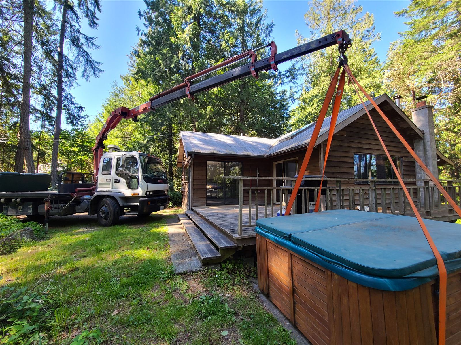 Crane lifting a hot tub beside a cedar house