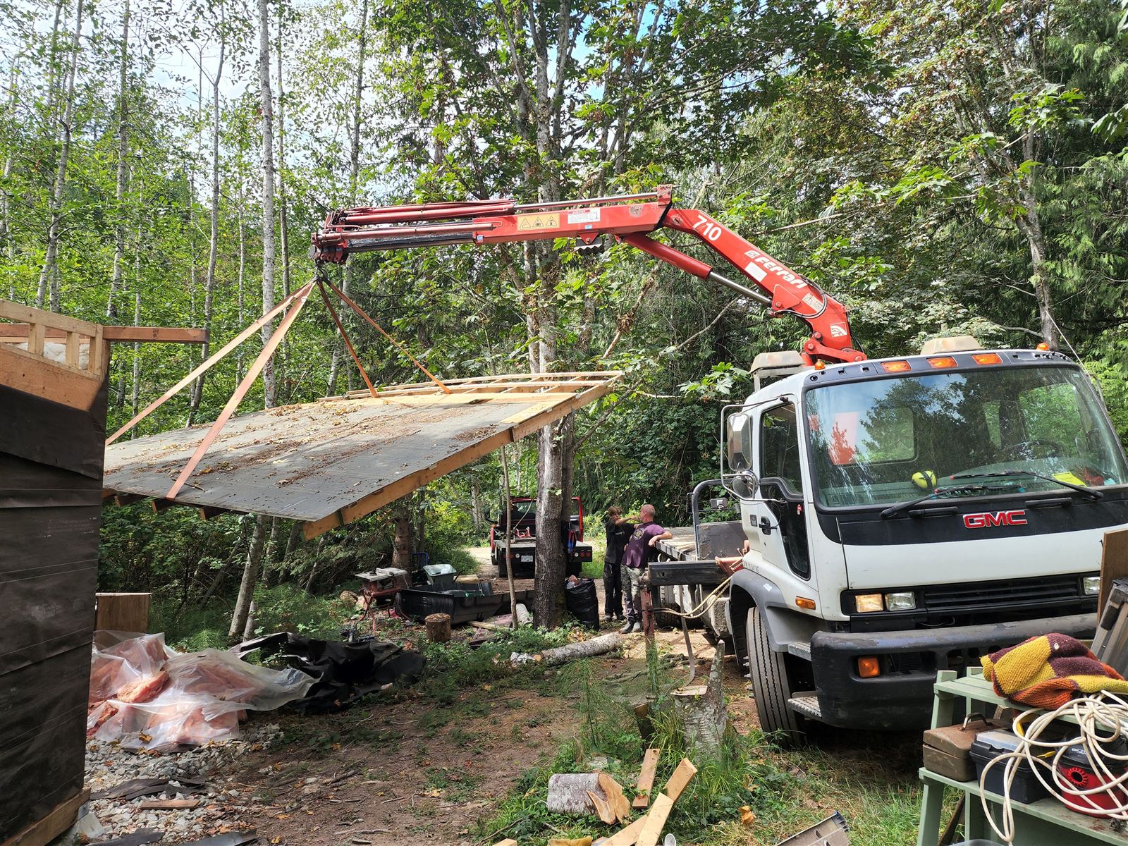 Crane lifting roofing panels next to a shed