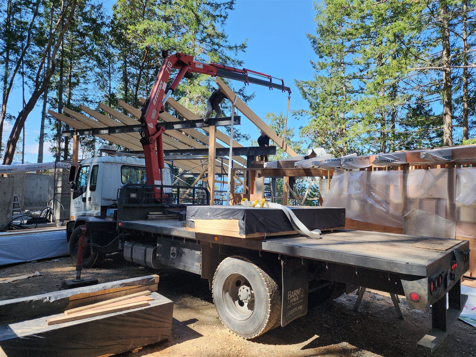 Truck deck loaded with timber beams beside a timber frame